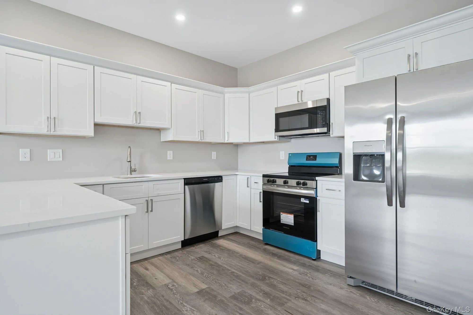 Kitchen with stainless steel appliances, white cabinets, wood finished floors, light countertops, and recessed lighting Kitchen with stainless steel appliances, white cabinets, wood finished floors, light countertops, and recessed lighting