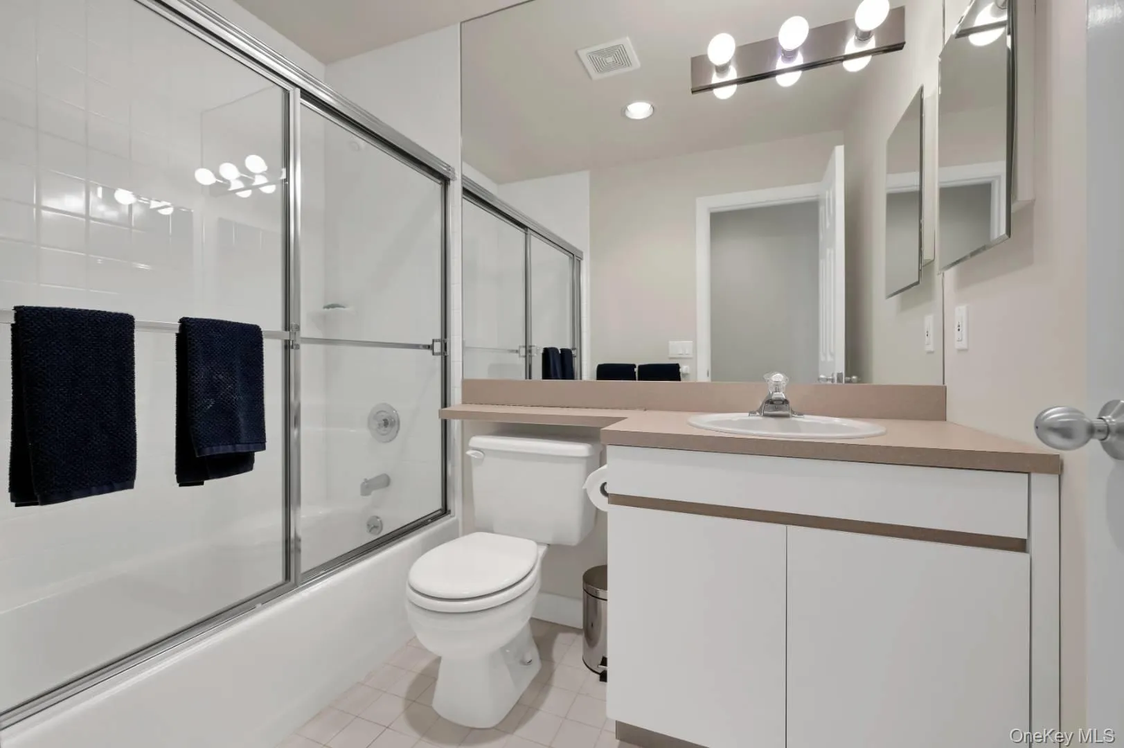 Full bath with visible vents, toilet, shower / bath combination with glass door, tile patterned floors, and vanity Full bath with visible vents, toilet, shower / bath combination with glass door, tile patterned floors, and vanity