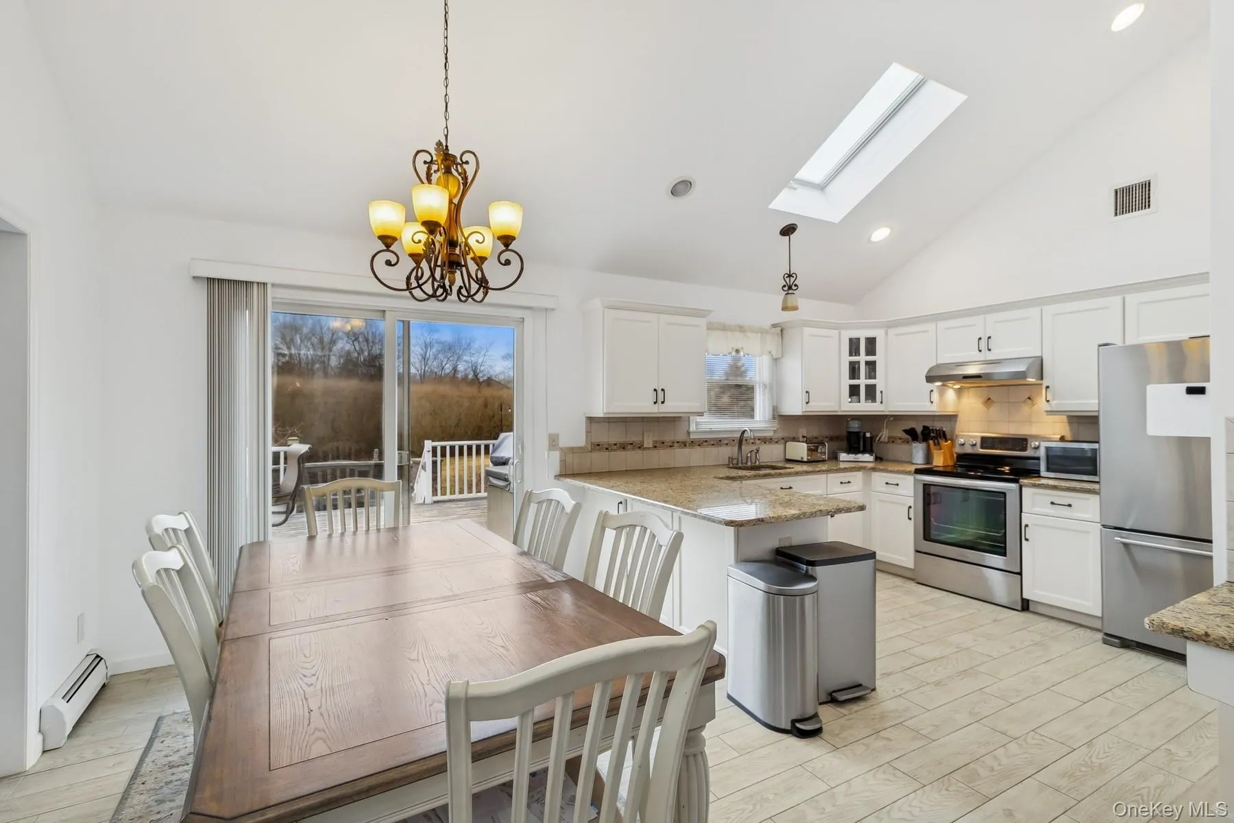 Kitchen featuring appliances with stainless steel finishes, a baseboard heating unit, a sink, a peninsula, and under cabinet range hood Kitchen featuring appliances with stainless steel finishes, a baseboard heating unit, a sink, a peninsula, and under cabinet range hood