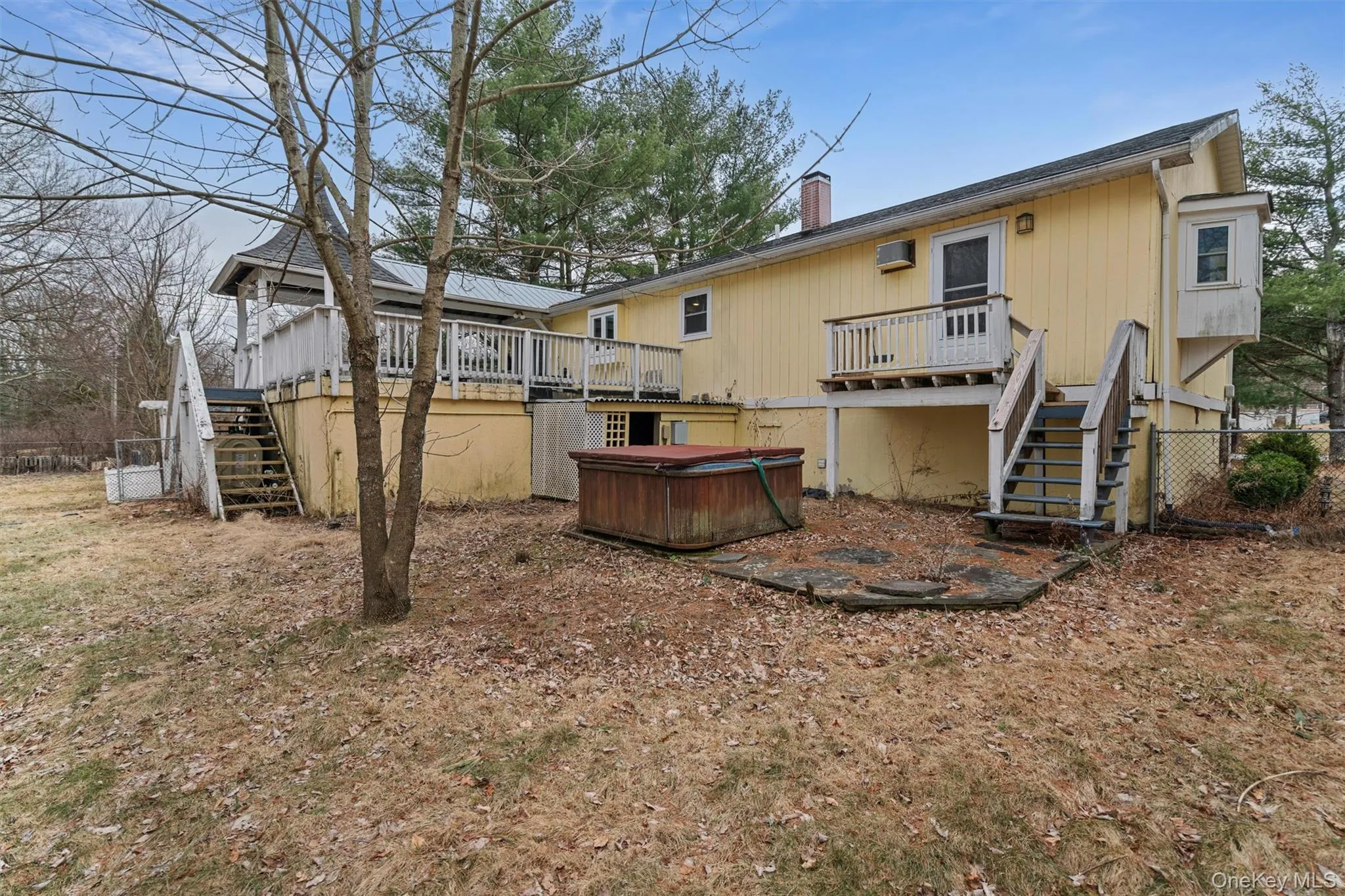 Rear view of house with stairway, a wooden deck, a chimney, and a hot tub Rear view of house with stairway, a wooden deck, a chimney, and a hot tub