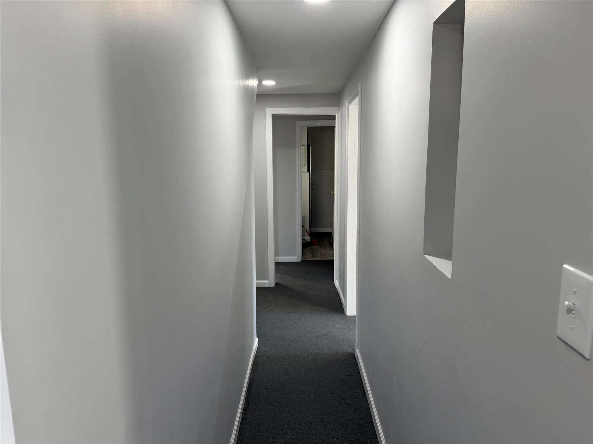Hallway featuring baseboards and dark colored carpet Hallway featuring baseboards and dark colored carpet