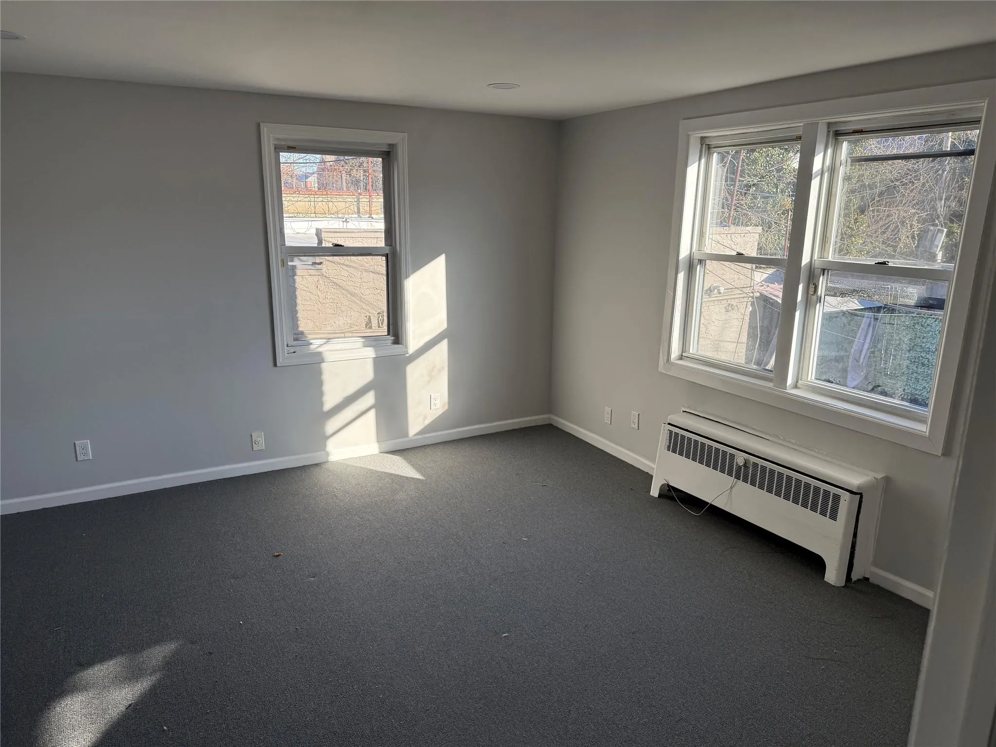 Spare room featuring dark colored carpet, baseboards, and radiator heating unit Spare room featuring dark colored carpet, baseboards, and radiator heating unit