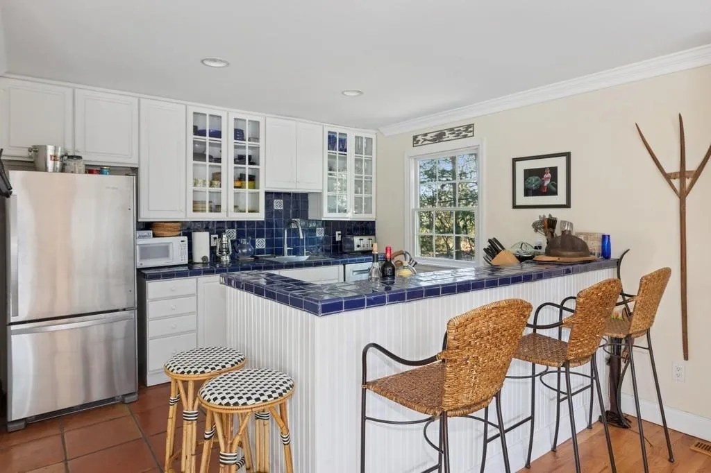 Kitchen featuring tile counters, white microwave, a kitchen breakfast bar, freestanding refrigerator, and backsplash Kitchen featuring tile counters, white microwave, a kitchen breakfast bar, freestanding refrigerator, and backsplash