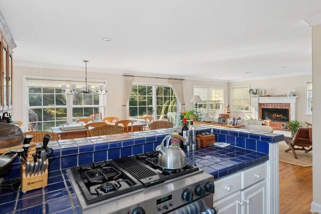 Kitchen with wood finished floors, ornamental molding, a brick fireplace, tile counters, and stainless steel range with gas stovetop Kitchen with wood finished floors, ornamental molding, a brick fireplace, tile counters, and stainless steel range with gas stovetop