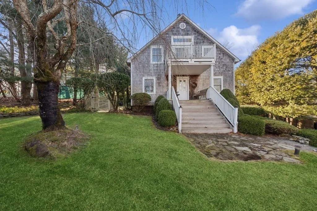 Shingle-style home featuring a balcony and a front lawn Shingle-style home featuring a balcony and a front lawn