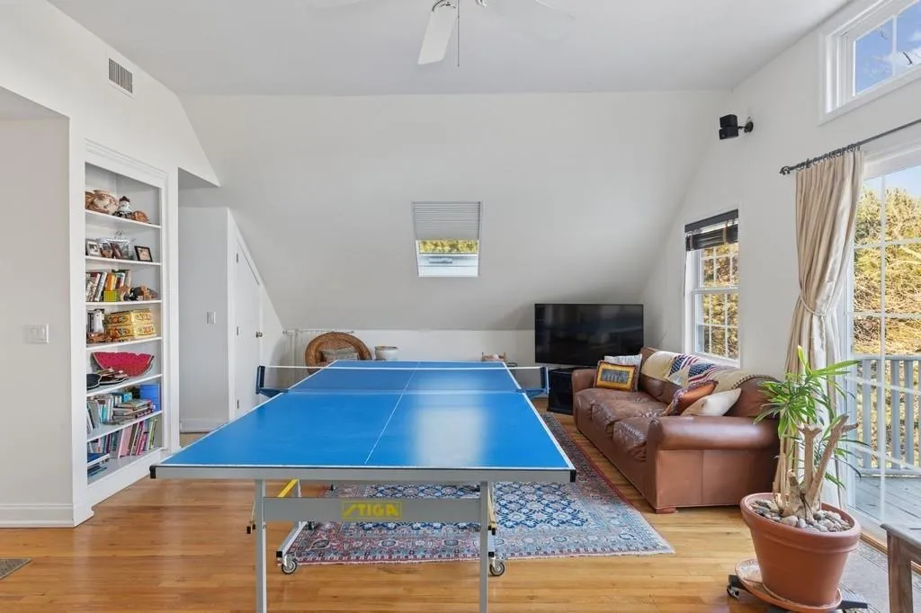 Playroom with lofted ceiling, ceiling fan, built in shelves, wood finished floors, and visible vents Playroom with lofted ceiling, ceiling fan, built in shelves, wood finished floors, and visible vents