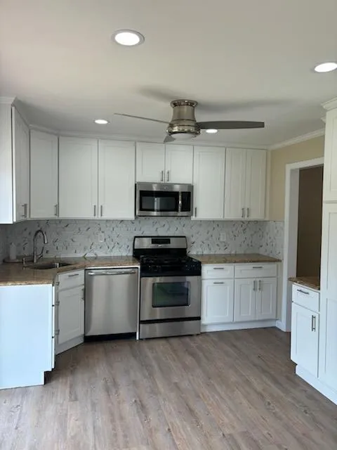 Kitchen with decorative backsplash, appliances with stainless steel finishes, a ceiling fan, ornamental molding, and a sink Kitchen with decorative backsplash, appliances with stainless steel finishes, a ceiling fan, ornamental molding, and a sink