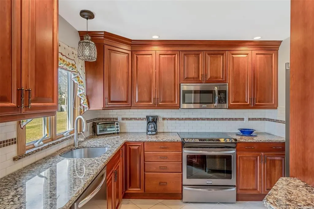 Kitchen with tasteful backsplash, decorative light fixtures, light stone countertops, stainless steel appliances, and a sink Kitchen with tasteful backsplash, decorative light fixtures, light stone countertops, stainless steel appliances, and a sink