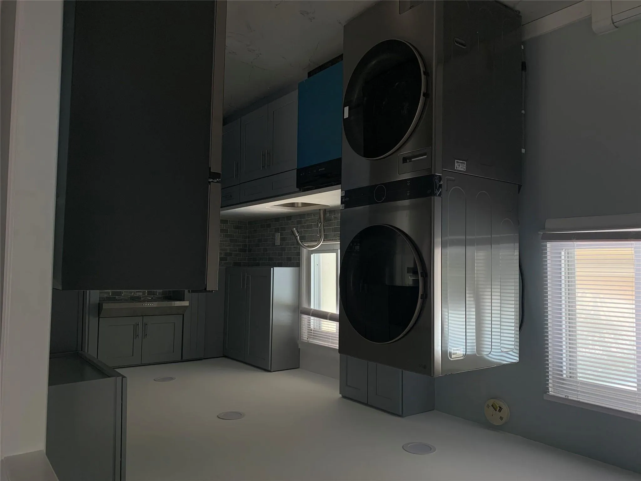 Kitchen with refrigerator, stacked washing machine and dryer, dishwashing machine, a baseboard heating unit, and light marble finish flooring Kitchen with refrigerator, stacked washing machine and dryer, dishwashing machine, a baseboard heating unit, and light marble finish flooring