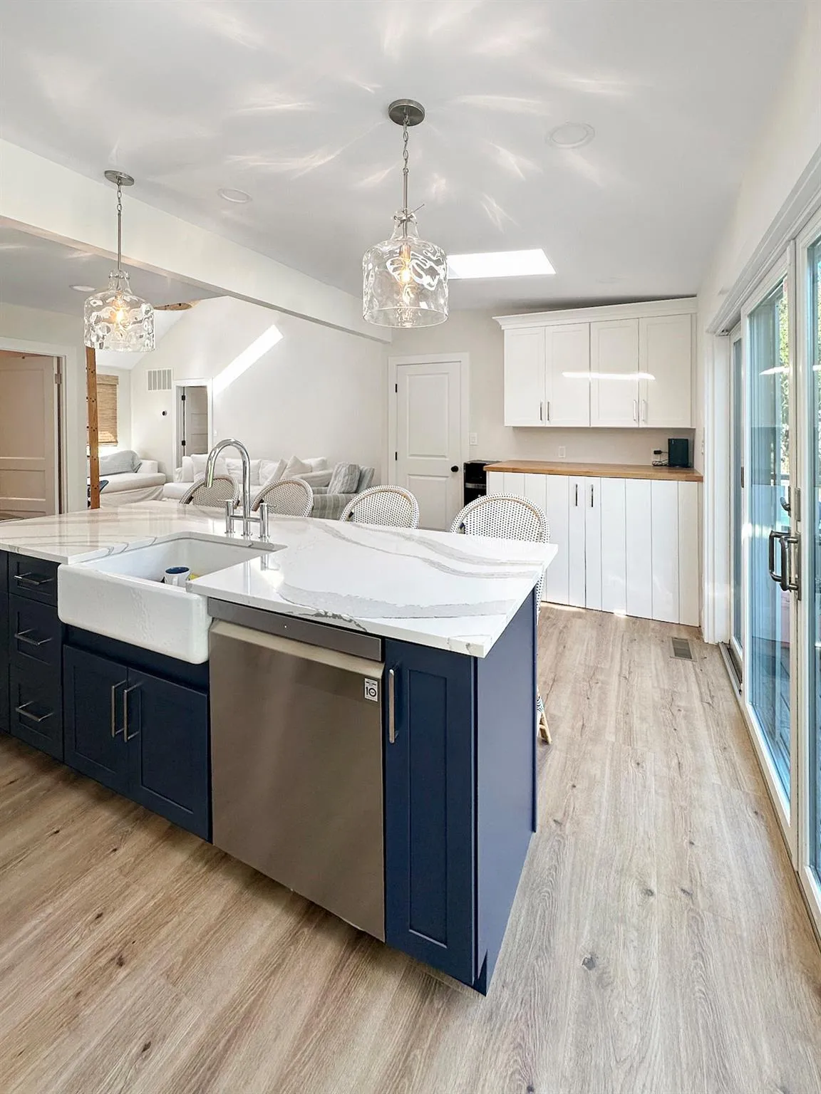 Kitchen with stainless steel dishwasher, light wood-style floors, open floor plan, white cabinets, and a sink Kitchen with stainless steel dishwasher, light wood-style floors, open floor plan, white cabinets, and a sink
