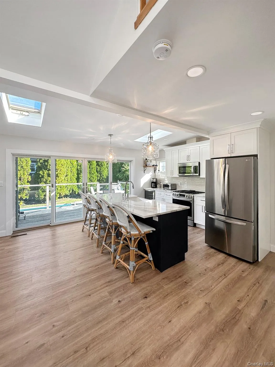 Kitchen featuring a skylight, white cabinets, decorative backsplash, stainless steel appliances, and a sink Kitchen featuring a skylight, white cabinets, decorative backsplash, stainless steel appliances, and a sink