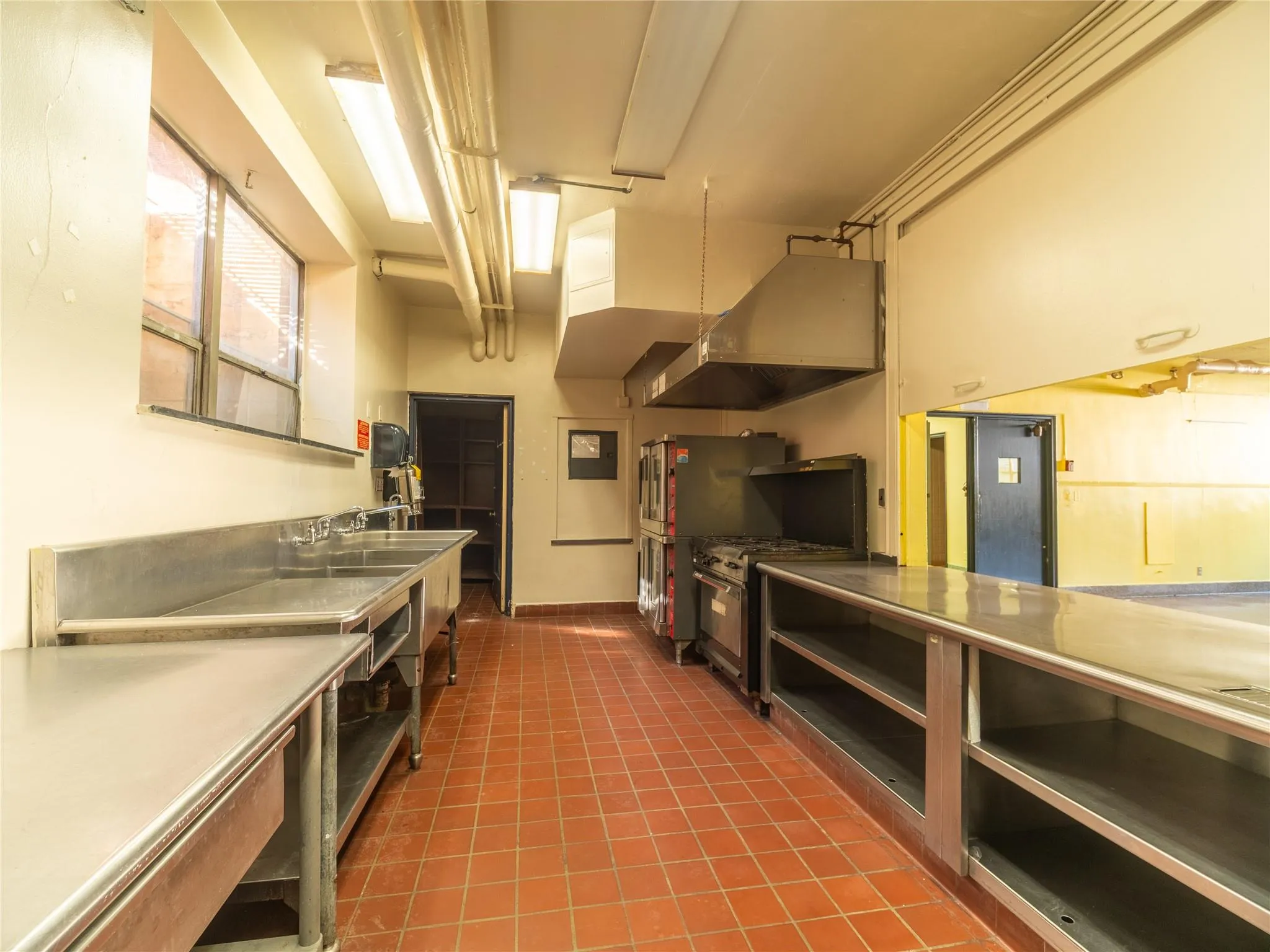 Kitchen featuring stainless steel appliances, under cabinet range hood, dark tile patterned flooring, a sink, and open shelves Kitchen featuring stainless steel appliances, under cabinet range hood, dark tile patterned flooring, a sink, and open shelves