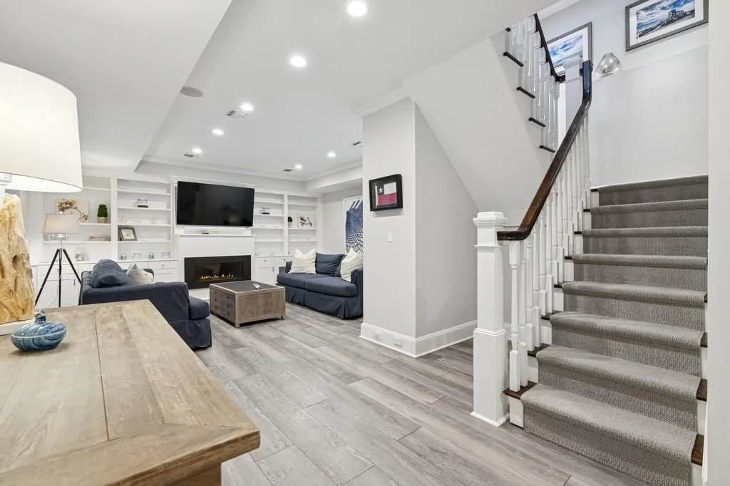 Living room featuring a warm lit fireplace, recessed lighting, crown molding, light wood finished floors, and baseboards Living room featuring a warm lit fireplace, recessed lighting, crown molding, light wood finished floors, and baseboards