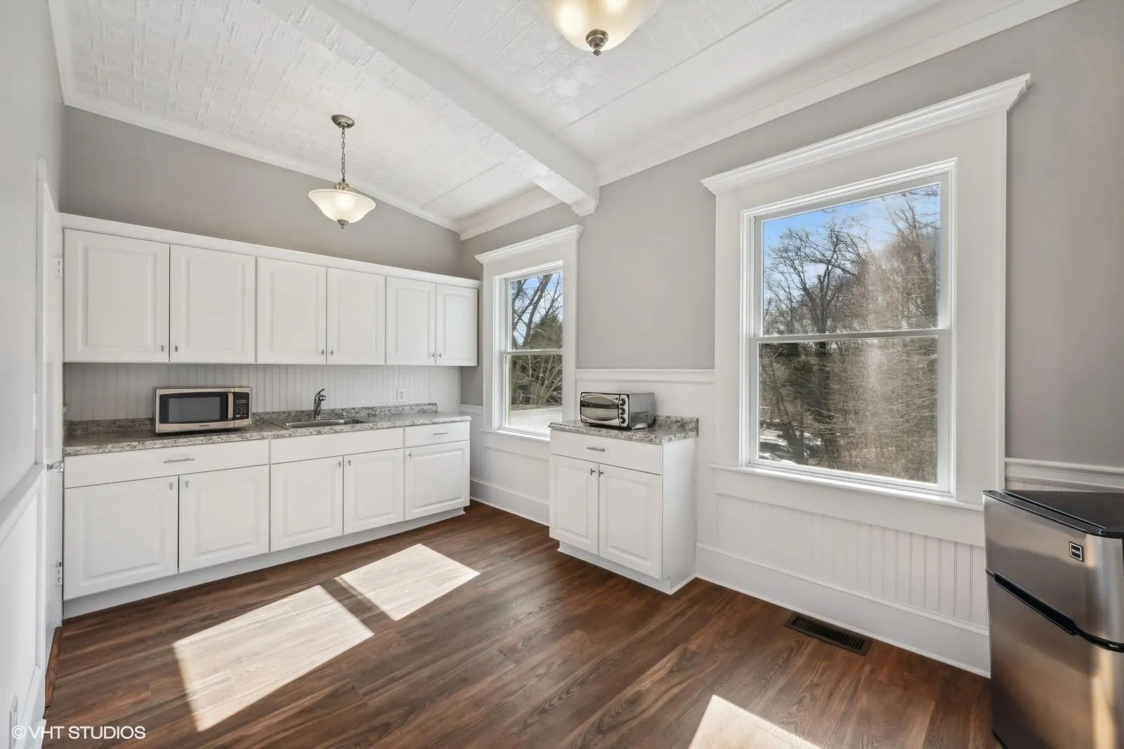 Kitchen with stainless steel microwave, dark wood-style flooring, a sink, white cabinets, and light stone countertops Kitchen with stainless steel microwave, dark wood-style flooring, a sink, white cabinets, and light stone countertops