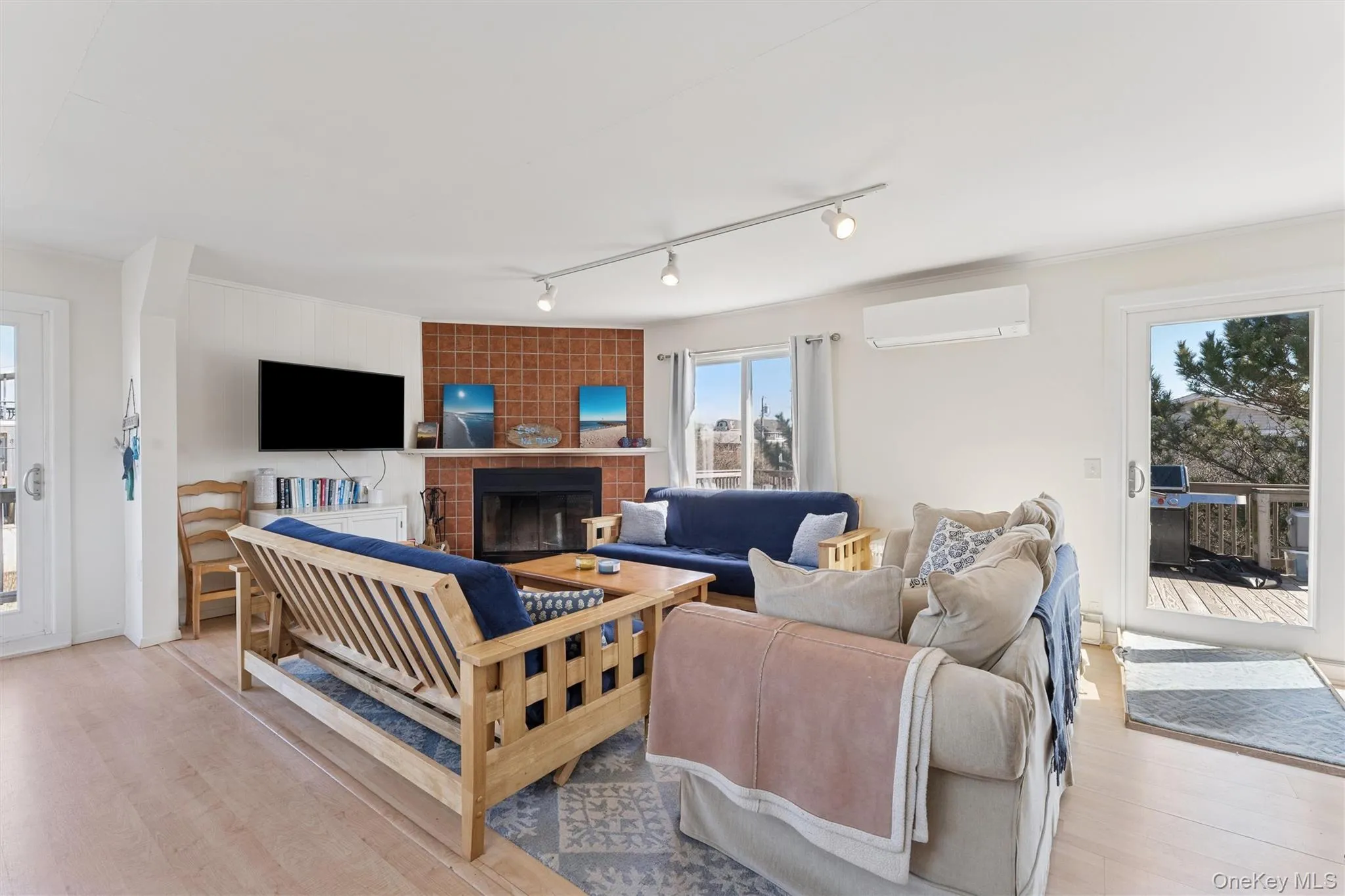 Living room with light wood-style flooring, a wall mounted air conditioner, and a large fireplace Living room with light wood-style flooring, a wall mounted air conditioner, and a large fireplace