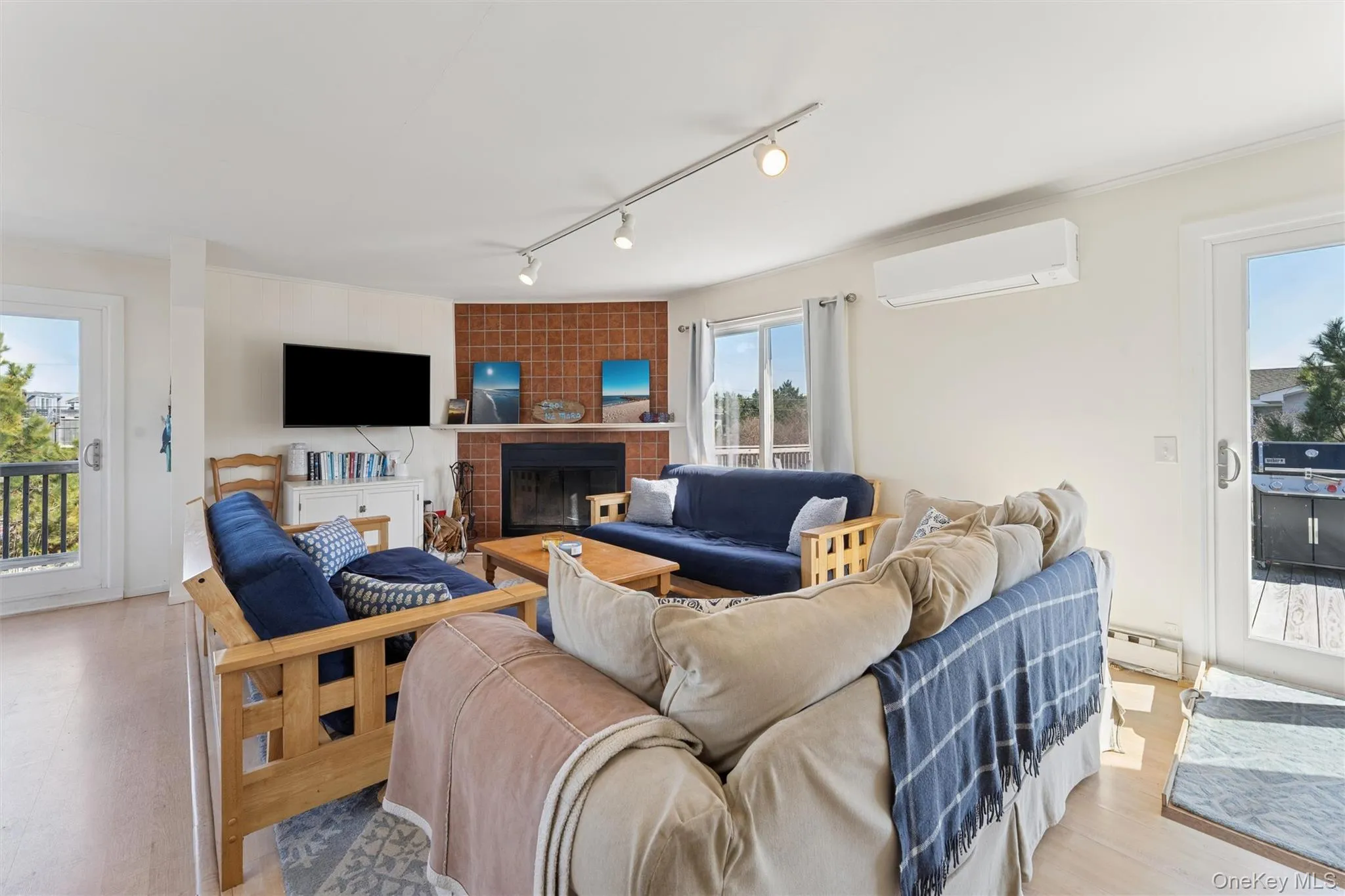 Living area featuring a baseboard heating unit, light wood finished floors, a tile fireplace, and a wall mounted AC Living area featuring a baseboard heating unit, light wood finished floors, a tile fireplace, and a wall mounted AC