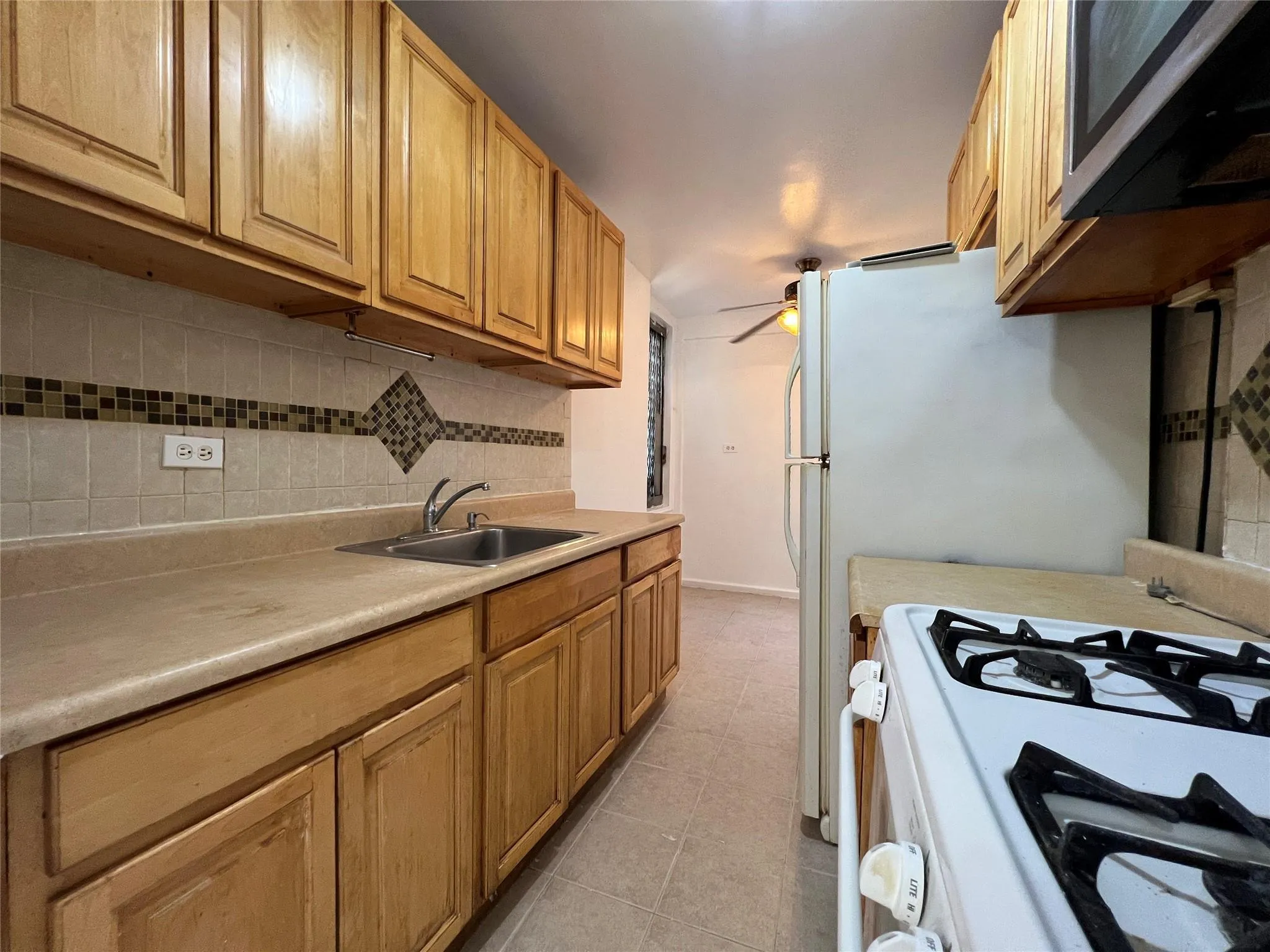 Kitchen with a ceiling fan, a sink, stainless steel microwave, tasteful backsplash, and white gas range oven Kitchen with a ceiling fan, a sink, stainless steel microwave, tasteful backsplash, and white gas range oven