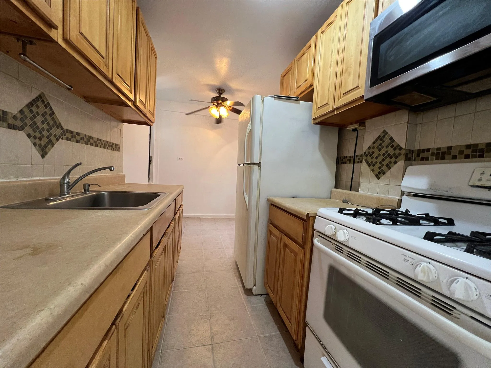 Kitchen with light tile patterned floors, ceiling fan, a sink, stainless steel microwave, and white gas range Kitchen with light tile patterned floors, ceiling fan, a sink, stainless steel microwave, and white gas range