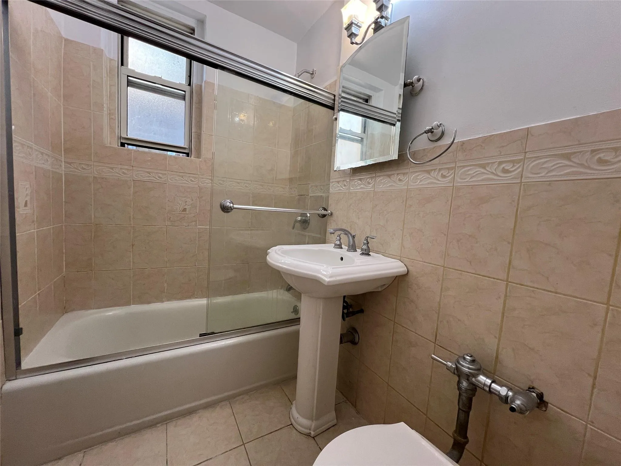 Full bathroom featuring tile patterned floors, toilet, radiator heating unit, combined bath / shower with glass door, and tile walls Full bathroom featuring tile patterned floors, toilet, radiator heating unit, combined bath / shower with glass door, and tile walls