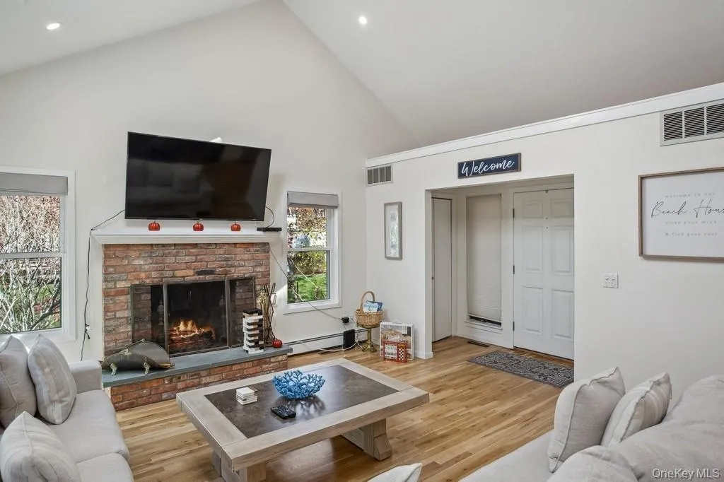 Living area with visible vents, a fireplace, high vaulted ceiling, and light wood-style floors Living area with visible vents, a fireplace, high vaulted ceiling, and light wood-style floors