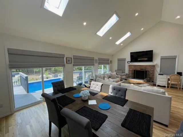 Dining space featuring a skylight, a brick fireplace, high vaulted ceiling, light wood-style floors, and recessed lighting Dining space featuring a skylight, a brick fireplace, high vaulted ceiling, light wood-style floors, and recessed lighting