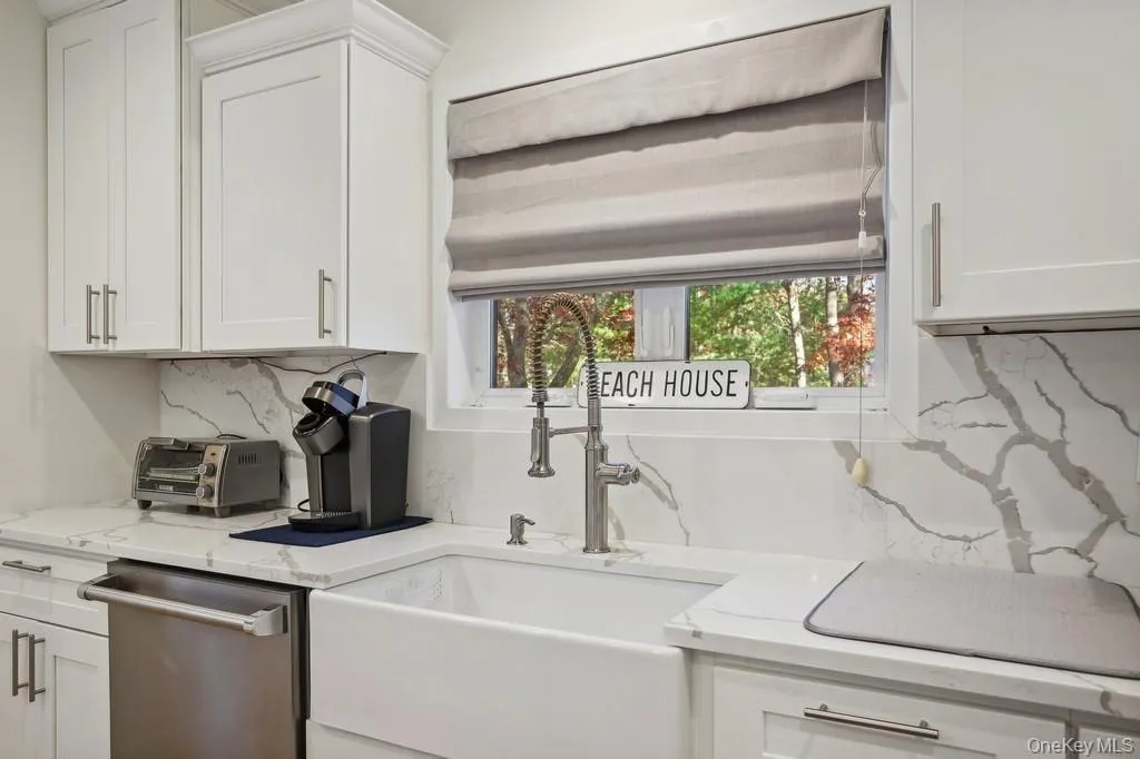 Kitchen with tasteful backsplash, white cabinets, dishwasher, and a sink Kitchen with tasteful backsplash, white cabinets, dishwasher, and a sink