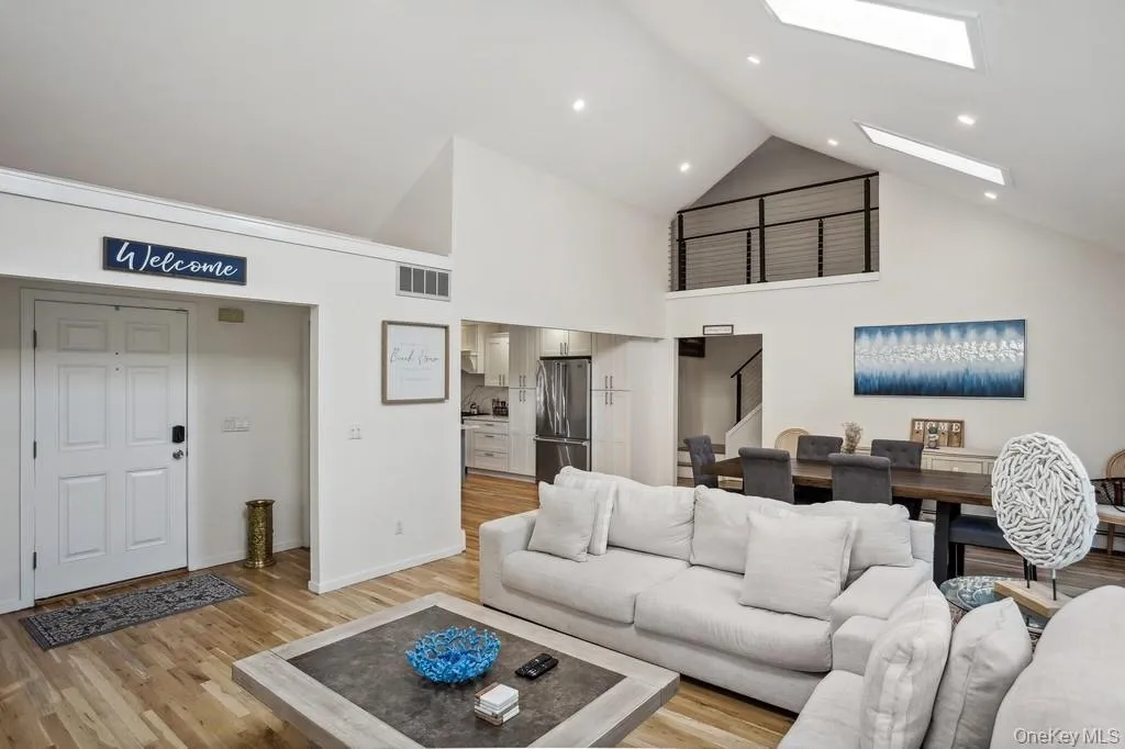 Living room with visible vents, high vaulted ceiling, stairway, light wood-style floors, and a skylight Living room with visible vents, high vaulted ceiling, stairway, light wood-style floors, and a skylight