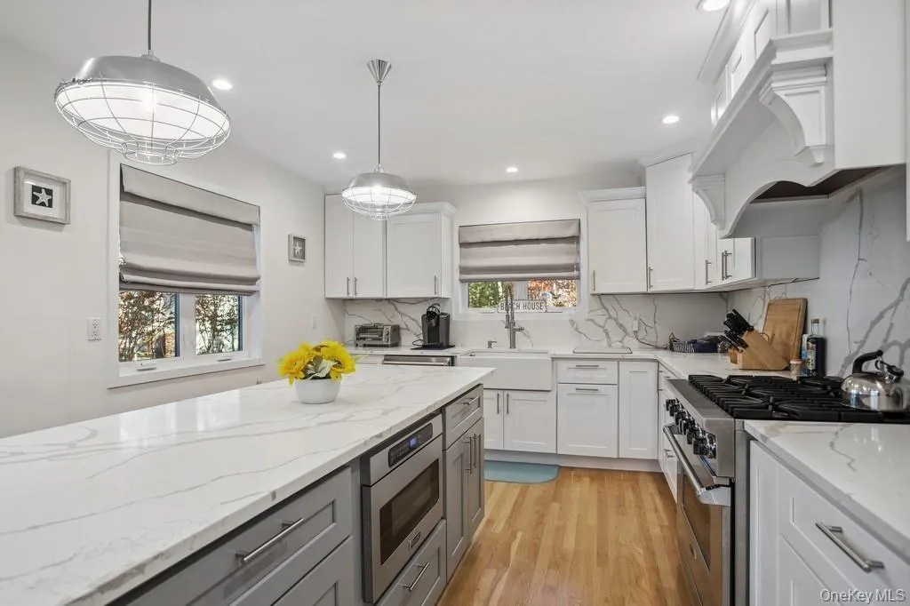 Kitchen with light wood-style flooring, a sink, custom range hood, appliances with stainless steel finishes, and backsplash Kitchen with light wood-style flooring, a sink, custom range hood, appliances with stainless steel finishes, and backsplash