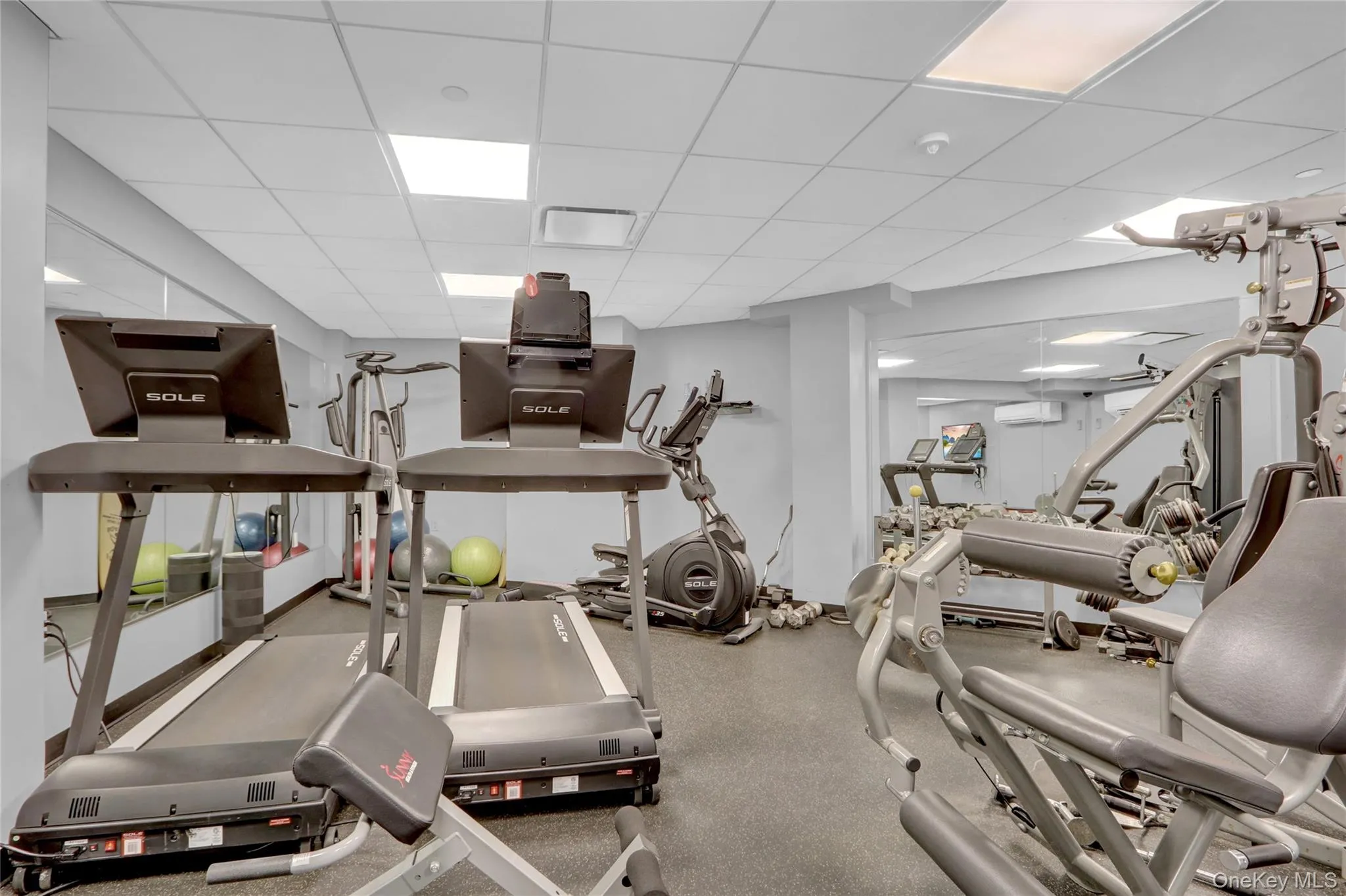 Exercise room featuring a drop ceiling, an AC wall unit, and visible vents Exercise room featuring a drop ceiling, an AC wall unit, and visible vents