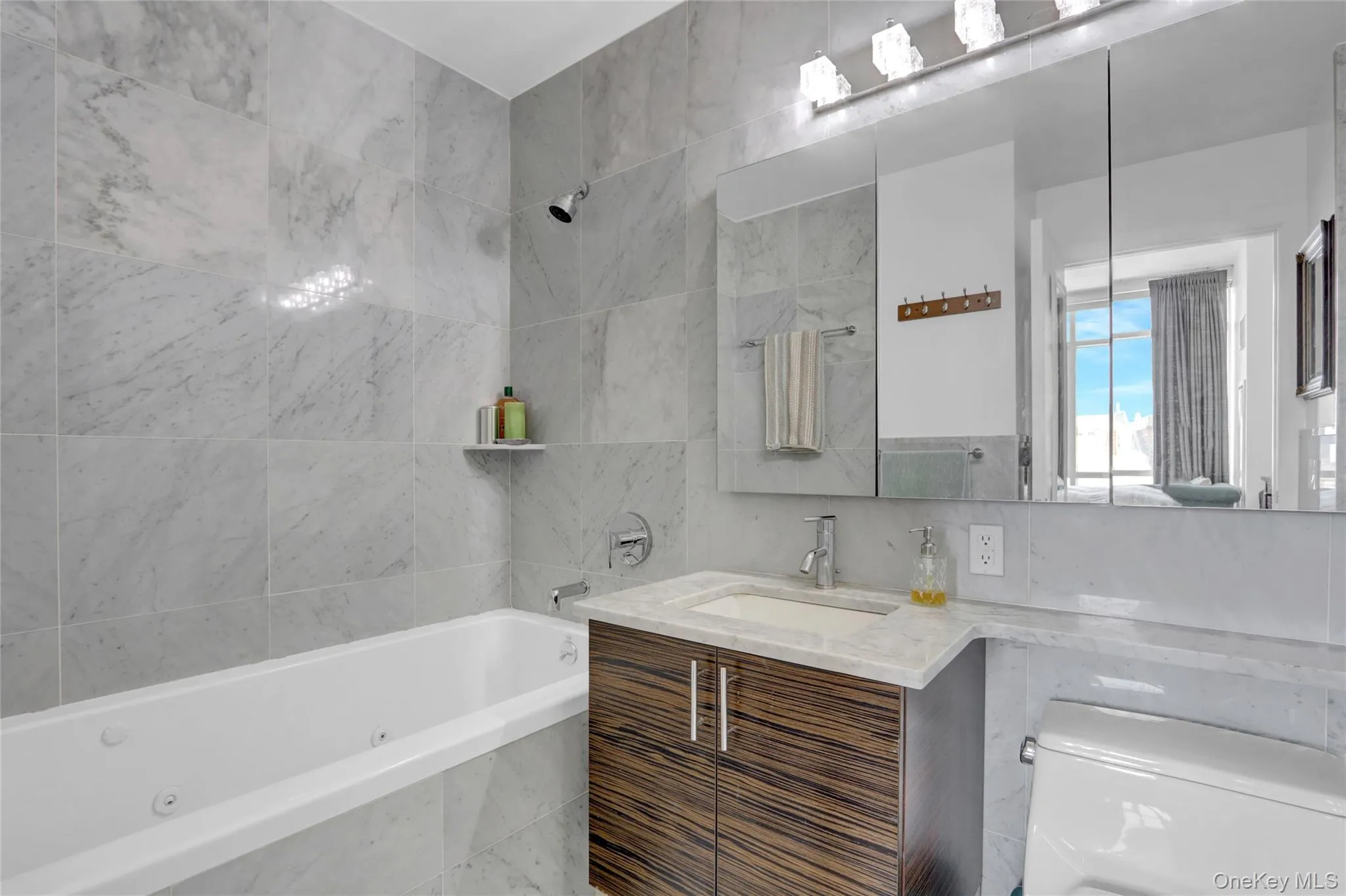 Bathroom with vanity, a combined bath / shower with jetted tub, tile walls, toilet, and backsplash Bathroom with vanity, a combined bath / shower with jetted tub, tile walls, toilet, and backsplash