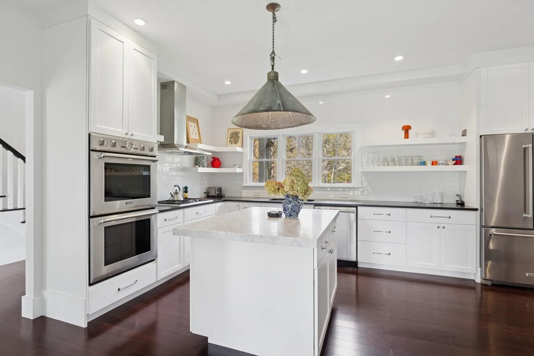 Kitchen featuring open shelves, wall chimney exhaust hood, appliances with stainless steel finishes, and dark wood-type flooring Kitchen featuring open shelves, wall chimney exhaust hood, appliances with stainless steel finishes, and dark wood-type flooring
