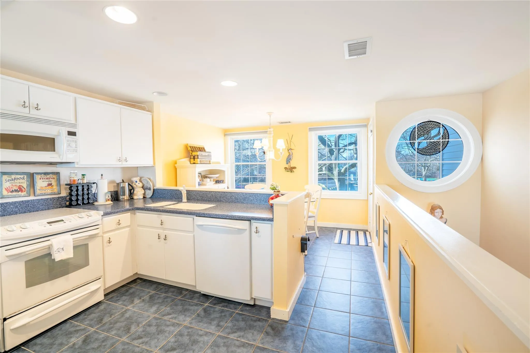 Kitchen featuring visible vents, dark tile patterned floors, a sink, white appliances, and a peninsula Kitchen featuring visible vents, dark tile patterned floors, a sink, white appliances, and a peninsula