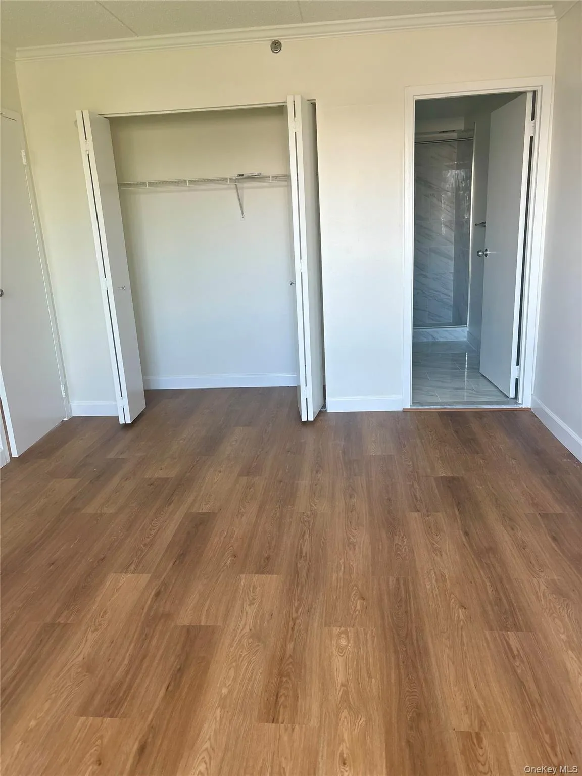 Unfurnished bedroom with a closet, crown molding, wood finished floors, and ensuite bathroom Unfurnished bedroom with a closet, crown molding, wood finished floors, and ensuite bathroom