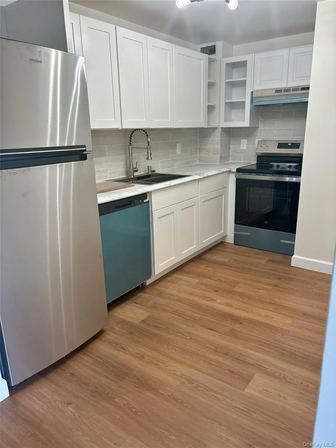 Kitchen featuring appliances with stainless steel finishes, under cabinet range hood, white cabinets, and light countertops Kitchen featuring appliances with stainless steel finishes, under cabinet range hood, white cabinets, and light countertops