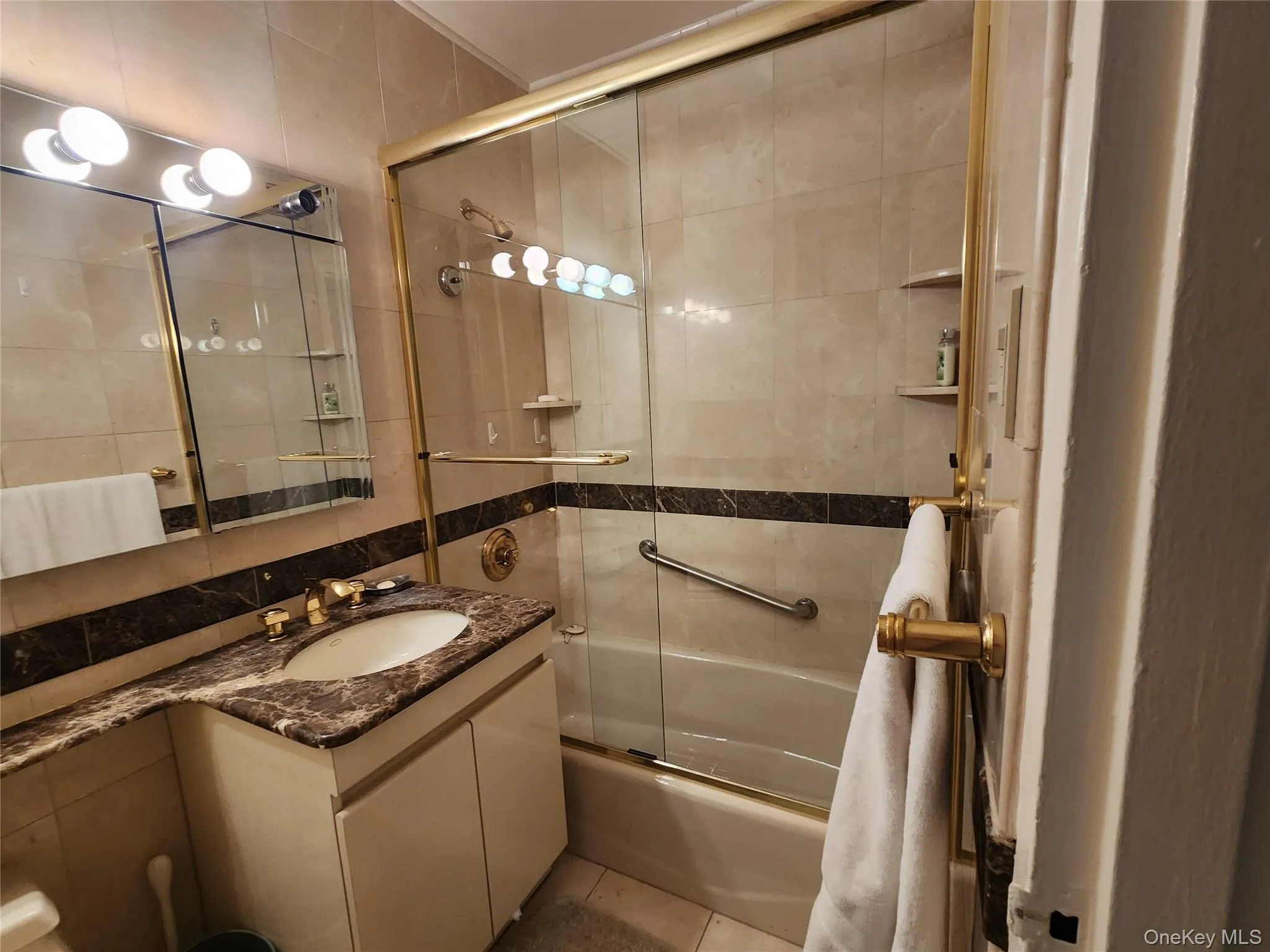 Full bathroom featuring combined bath / shower with glass door, tile walls, vanity, and tile patterned flooring Full bathroom featuring combined bath / shower with glass door, tile walls, vanity, and tile patterned flooring