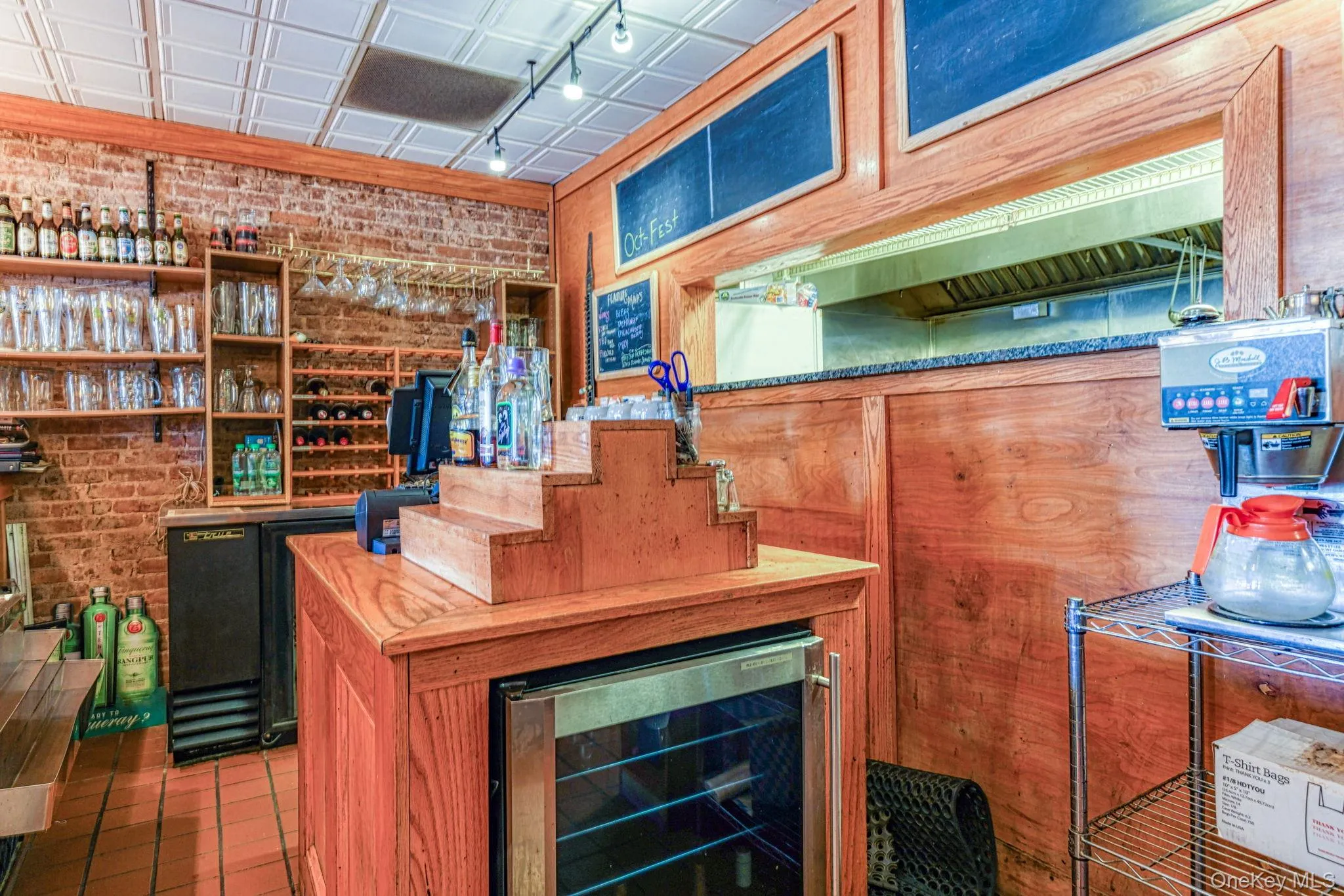 Bar with a dry bar, rail lighting, beverage cooler, and brick wall Bar with a dry bar, rail lighting, beverage cooler, and brick wall