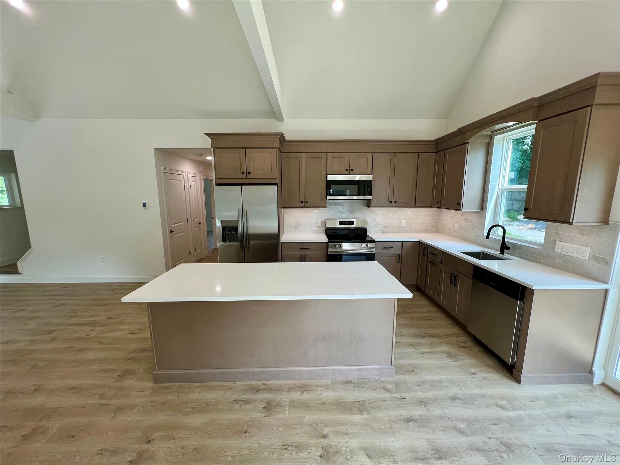 Kitchen with stainless steel appliances, a center island, tasteful backsplash, light wood-type flooring, and high vaulted ceiling Kitchen with stainless steel appliances, a center island, tasteful backsplash, light wood-type flooring, and high vaulted ceiling