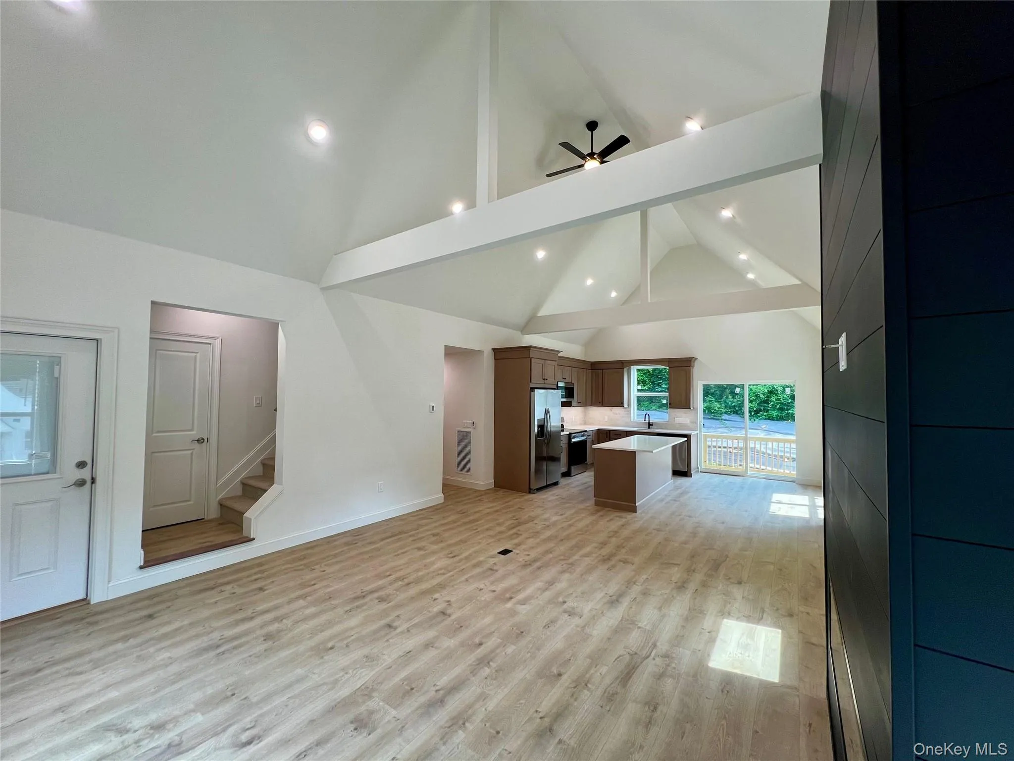 Unfurnished living room with beam ceiling, high vaulted ceiling, light wood finished floors, stairway, and a ceiling fan Unfurnished living room with beam ceiling, high vaulted ceiling, light wood finished floors, stairway, and a ceiling fan