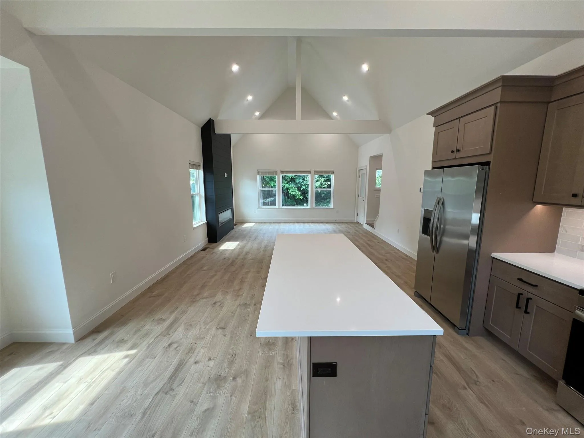 Kitchen with stainless steel fridge with ice dispenser, open floor plan, a center island, light countertops, and light wood-style floors Kitchen with stainless steel fridge with ice dispenser, open floor plan, a center island, light countertops, and light wood-style floors