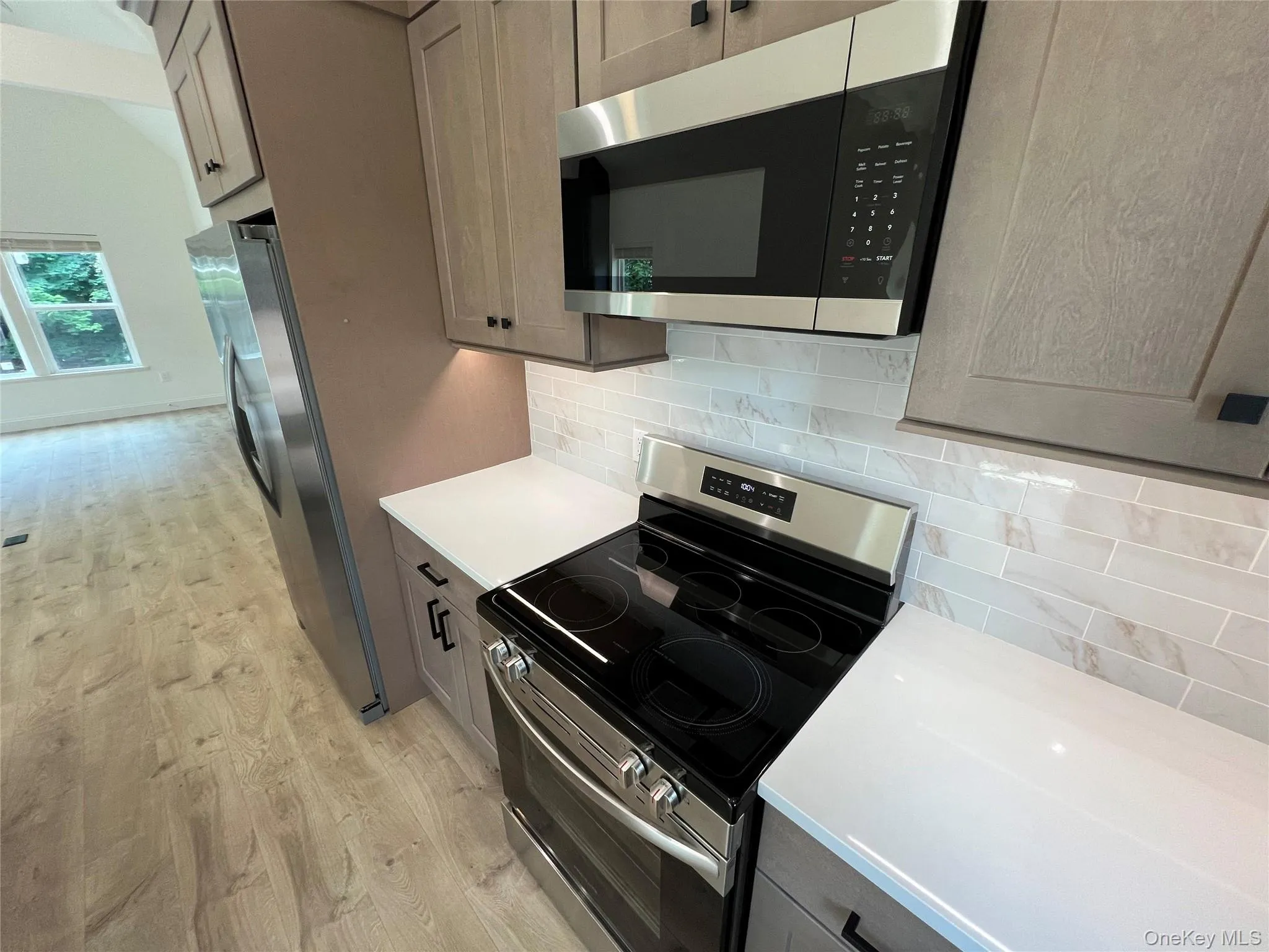 Kitchen featuring stainless steel appliances, light wood-type flooring, light countertops, and backsplash Kitchen featuring stainless steel appliances, light wood-type flooring, light countertops, and backsplash