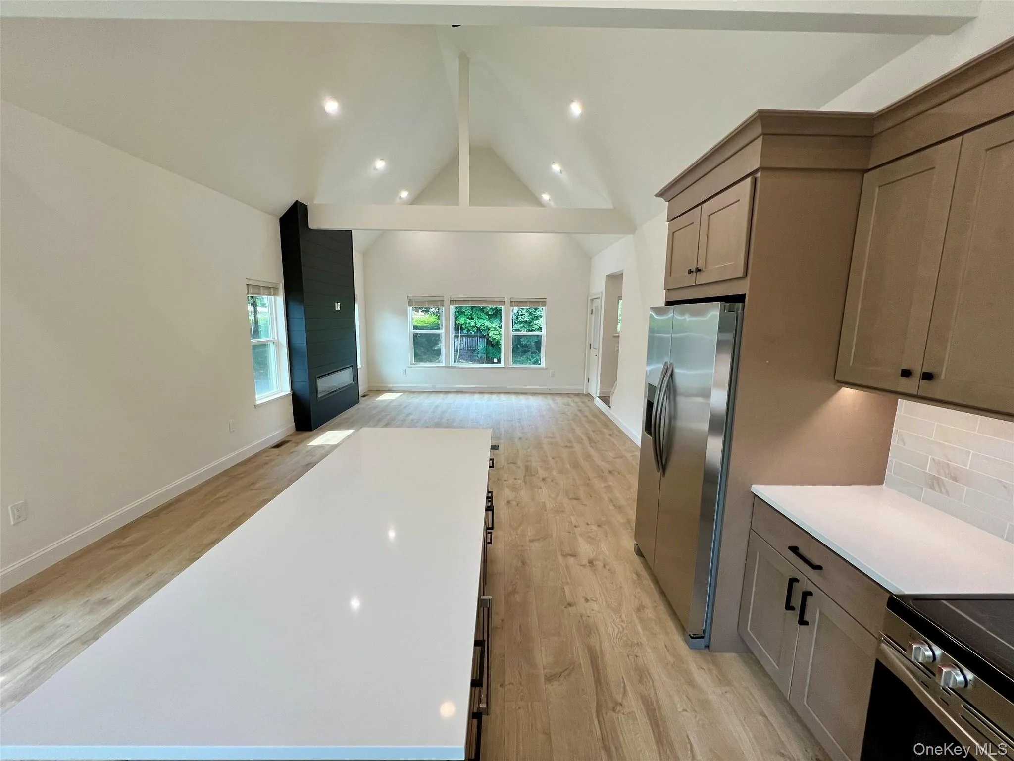 Kitchen featuring stainless steel appliances, open floor plan, tasteful backsplash, light wood-style flooring, and high vaulted ceiling Kitchen featuring stainless steel appliances, open floor plan, tasteful backsplash, light wood-style flooring, and high vaulted ceiling