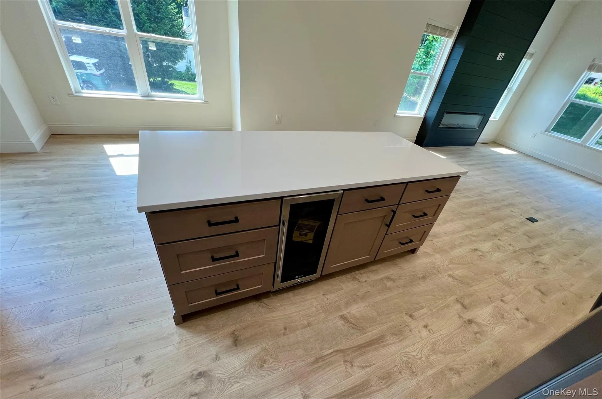 Bar featuring light wood-style floors, healthy amount of natural light, wine cooler, and a fireplace Bar featuring light wood-style floors, healthy amount of natural light, wine cooler, and a fireplace