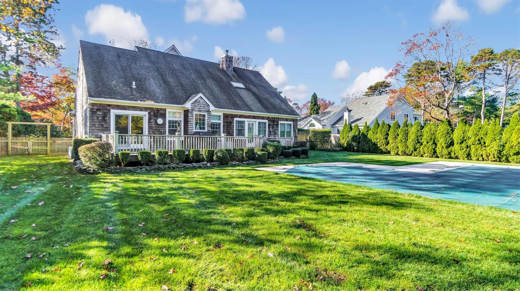 Rear view of house with a chimney, a wooden deck, a yard, and fence Rear view of house with a chimney, a wooden deck, a yard, and fence