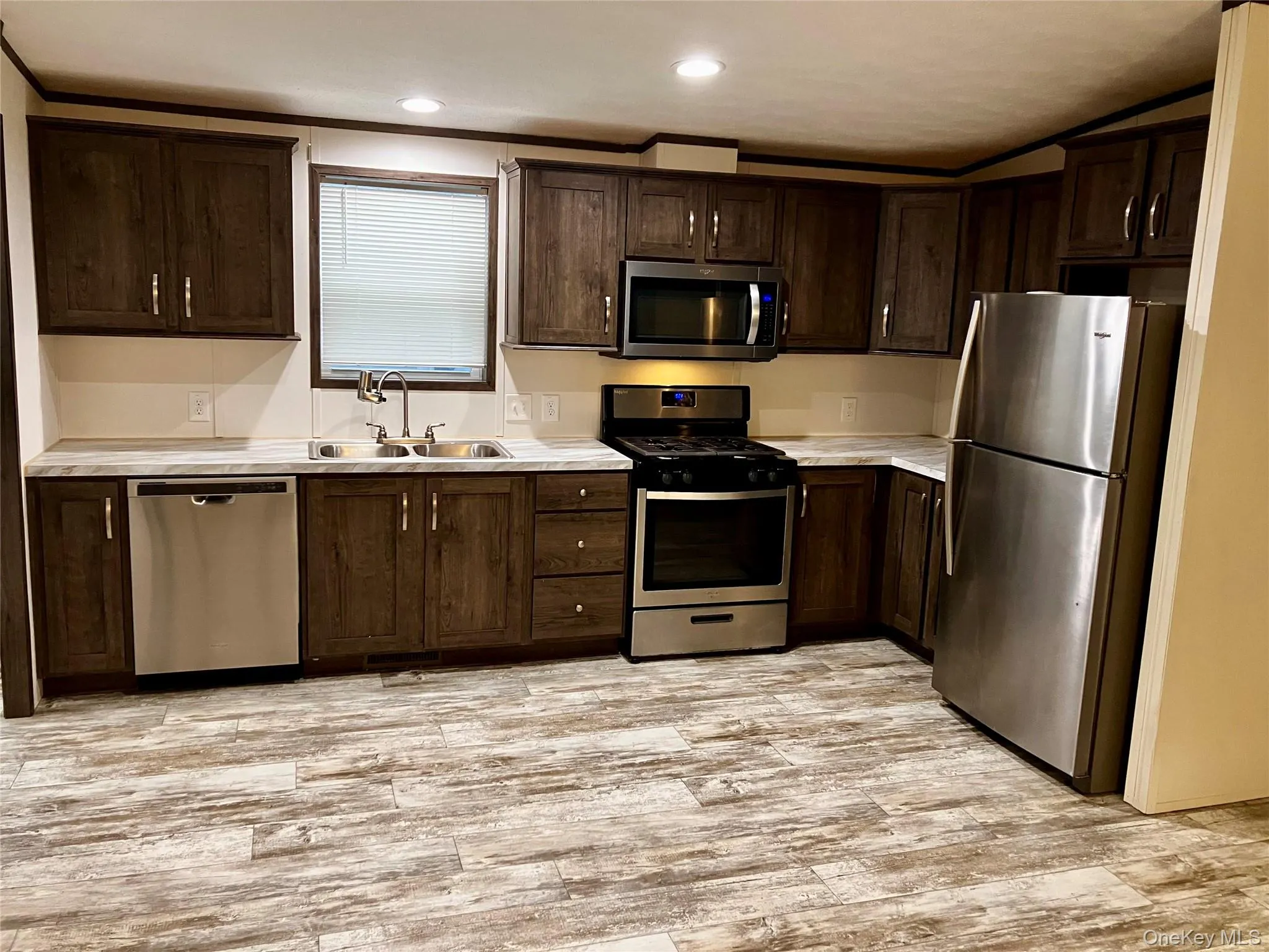 Kitchen with light countertops, light wood finished floors, dark brown cabinets, appliances with stainless steel finishes, and a sink Kitchen with light countertops, light wood finished floors, dark brown cabinets, appliances with stainless steel finishes, and a sink