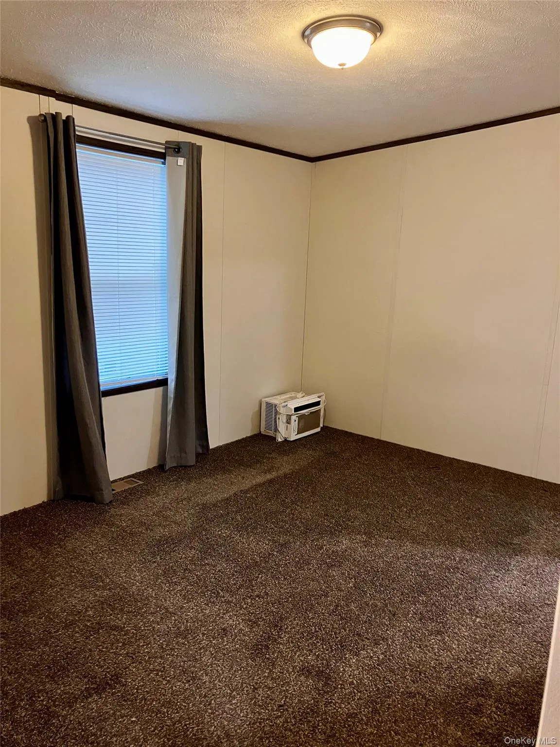 Carpeted empty room featuring a wall mounted AC and a textured ceiling Carpeted empty room featuring a wall mounted AC and a textured ceiling