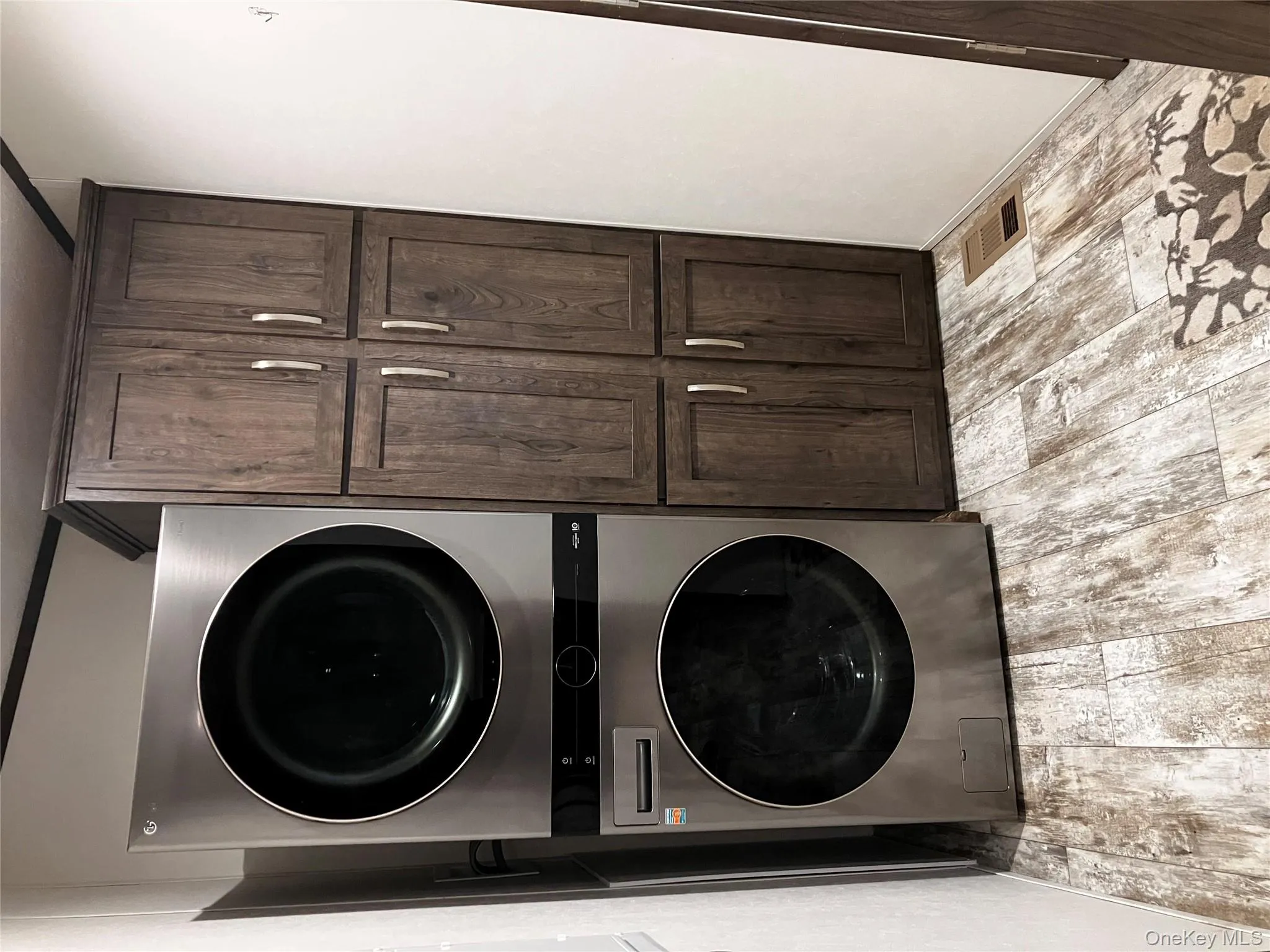 Washroom featuring wood finish floors, stacked washer and dryer, cabinet space, and visible vents Washroom featuring wood finish floors, stacked washer and dryer, cabinet space, and visible vents