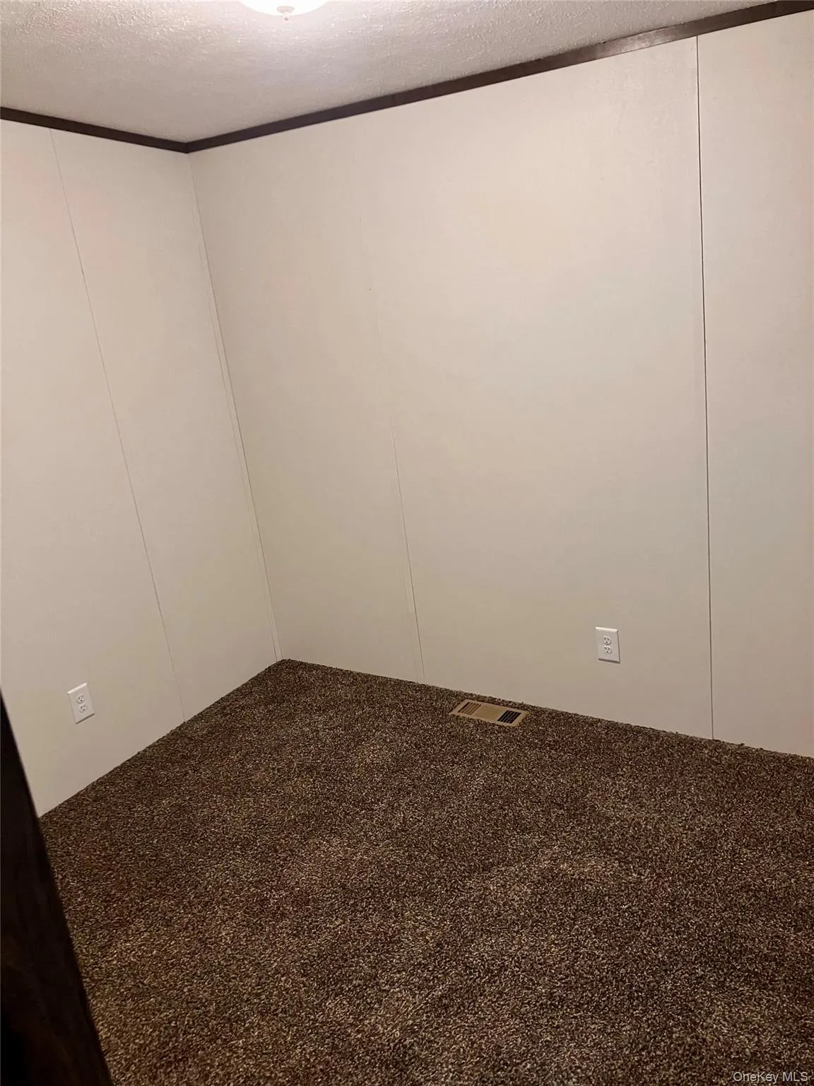 Carpeted empty room with visible vents, a decorative wall, and a textured ceiling Carpeted empty room with visible vents, a decorative wall, and a textured ceiling