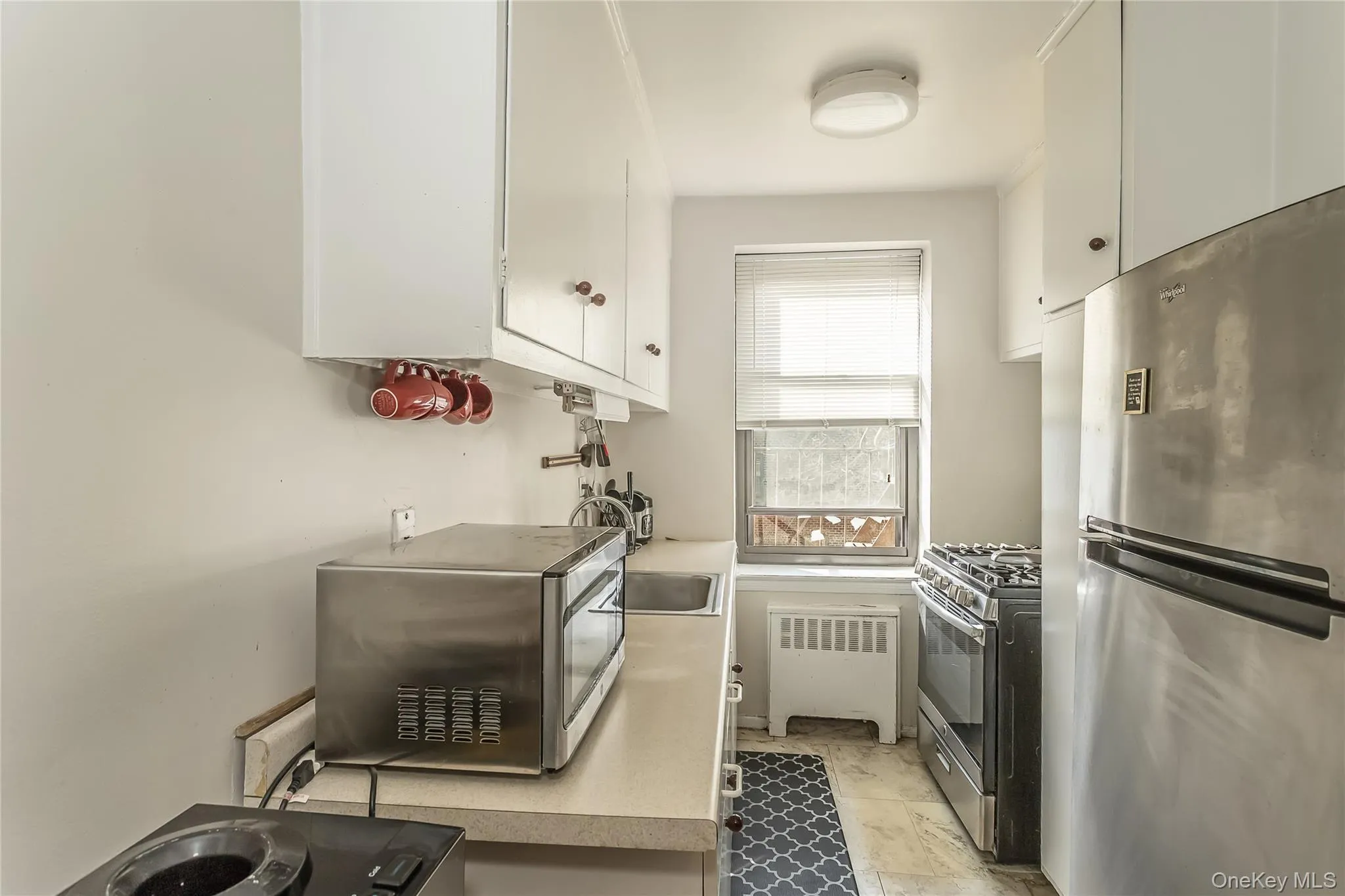 Kitchen with stainless steel appliances, light countertops, radiator heating unit, and white cabinetry Kitchen with stainless steel appliances, light countertops, radiator heating unit, and white cabinetry