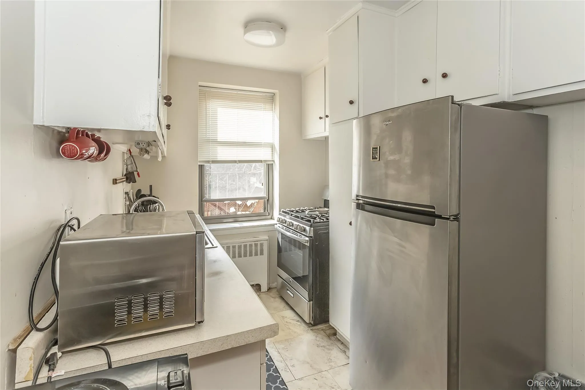 Kitchen with radiator, a toaster, light countertops, appliances with stainless steel finishes, and white cabinetry Kitchen with radiator, a toaster, light countertops, appliances with stainless steel finishes, and white cabinetry