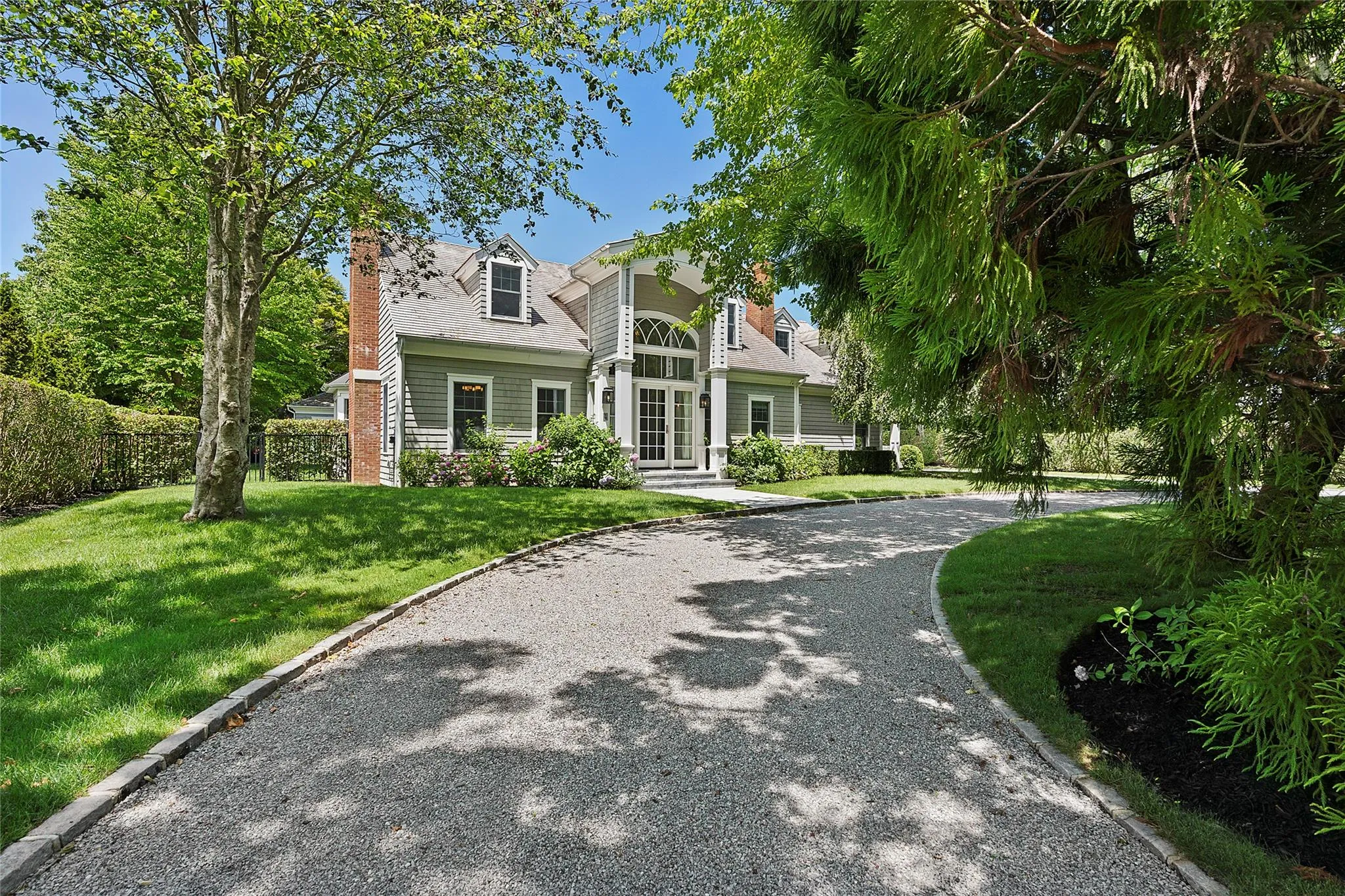 New england style home featuring a front yard, a chimney, and curved driveway New england style home featuring a front yard, a chimney, and curved driveway